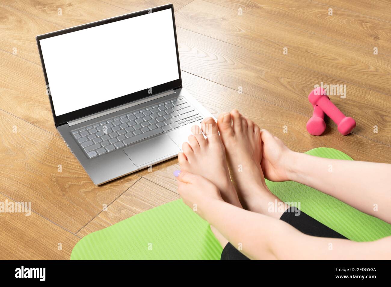 Posez une femme sportive en bonne santé assise sur un tapis dans la pose de Paschimottanasana, faisant des exercices de respiration, regardant les cours de yoga en ligne sur ordinateur portable maquette. Activé Banque D'Images
