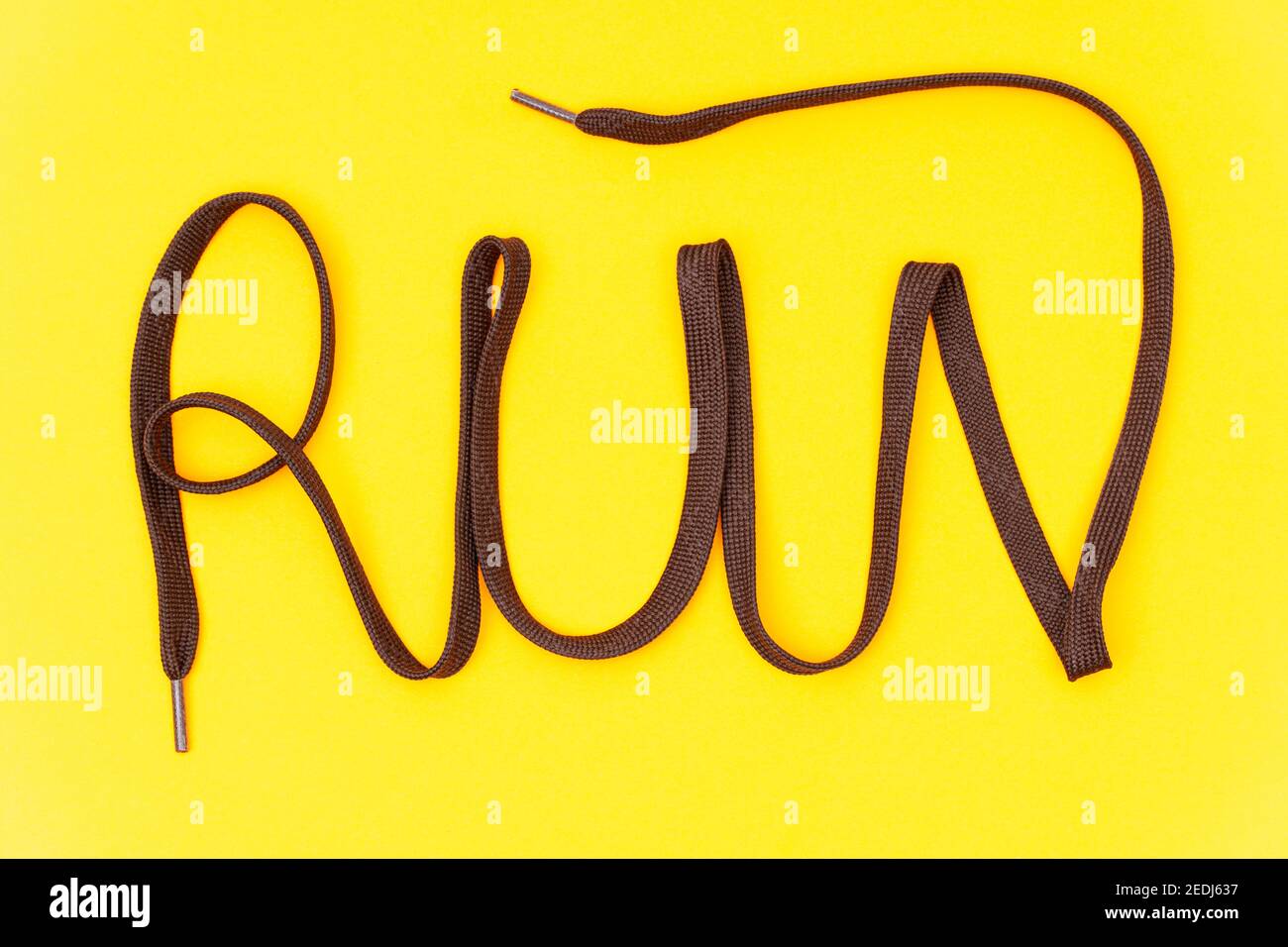 Mot « run » fait de lacets athlétiques marron sur fond jaune. Composition créative de la pose à plat. Banque D'Images