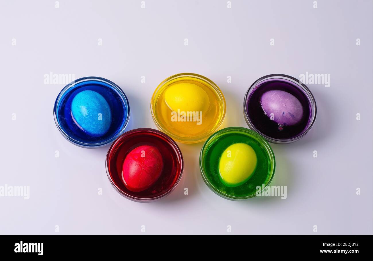 Les œufs blancs de poulet se trouvent dans des bols en verre avec de l'eau colorée sur un fond clair. Couleurs jaune, rouge, violet, vert, bleu. Étape 4 Banque D'Images