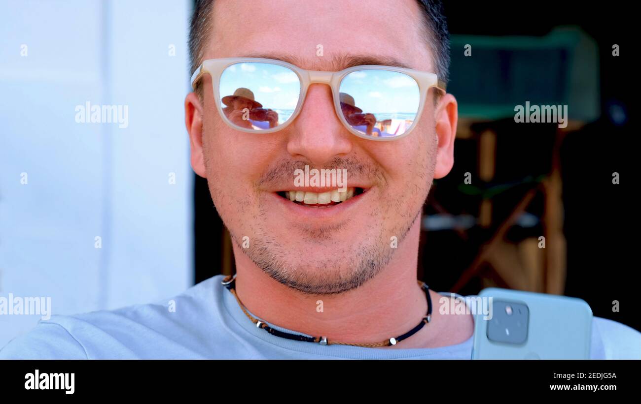 Positif jeune homme portant des lunettes de soleil miroir stylées souriant à attrayant femme réfléchissant dans des verres sur la plage de la mer vue proche Banque D'Images