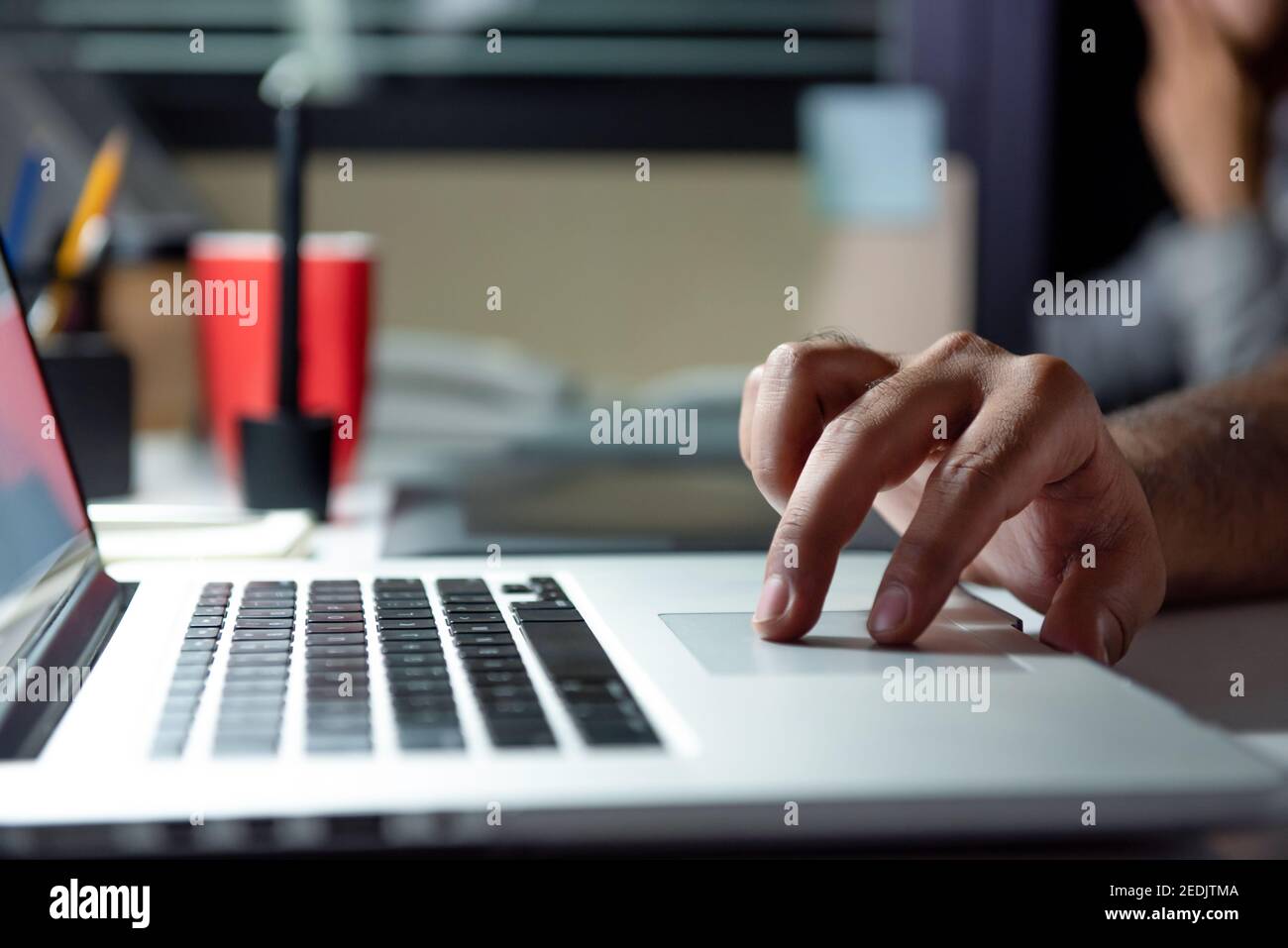 Main d'un homme utilisant un ordinateur portable travaillant des heures supplémentaires tard la nuit dans le bureau à son bureau Banque D'Images