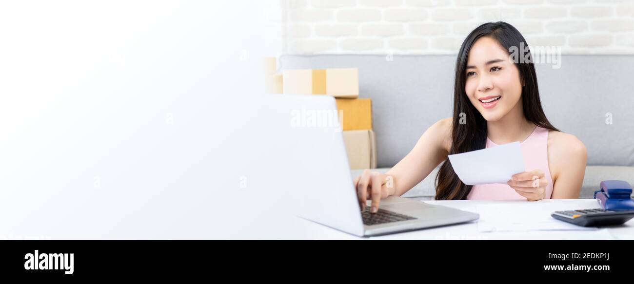 Femme asiatique entrepreneur ou vendeur en ligne freelance travaillant sur ordinateur portable vérifier commande sur Internet à la maison se préparant à la livraison, panoramique ba Banque D'Images