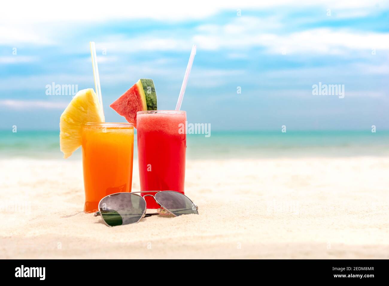Punch aux fruits tropicaux froids et colorés avec lunettes de soleil arrière-plan de plage de sable blanc d'été avec espace de copie Banque D'Images
