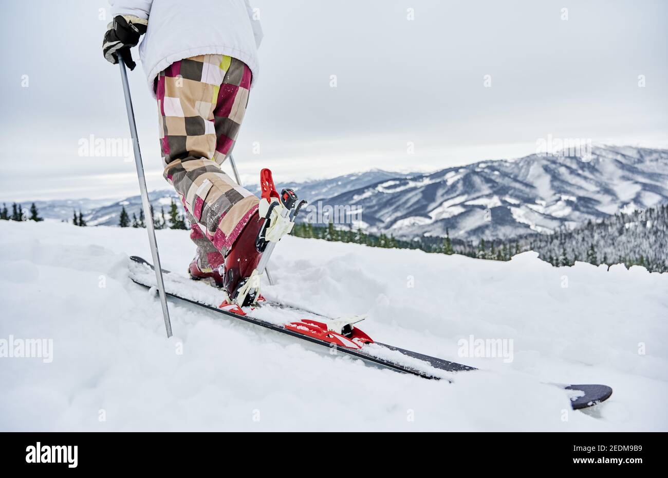 Gros plan sur le skieur alpin en hiver, pantalons de ski grimpant sur la colline enneigée avec de belles montagnes en arrière-plan. Homme à skis utilisant des bâtons de ski tout en marchant dans la neige blanche. Concept de ski et de sport. Banque D'Images