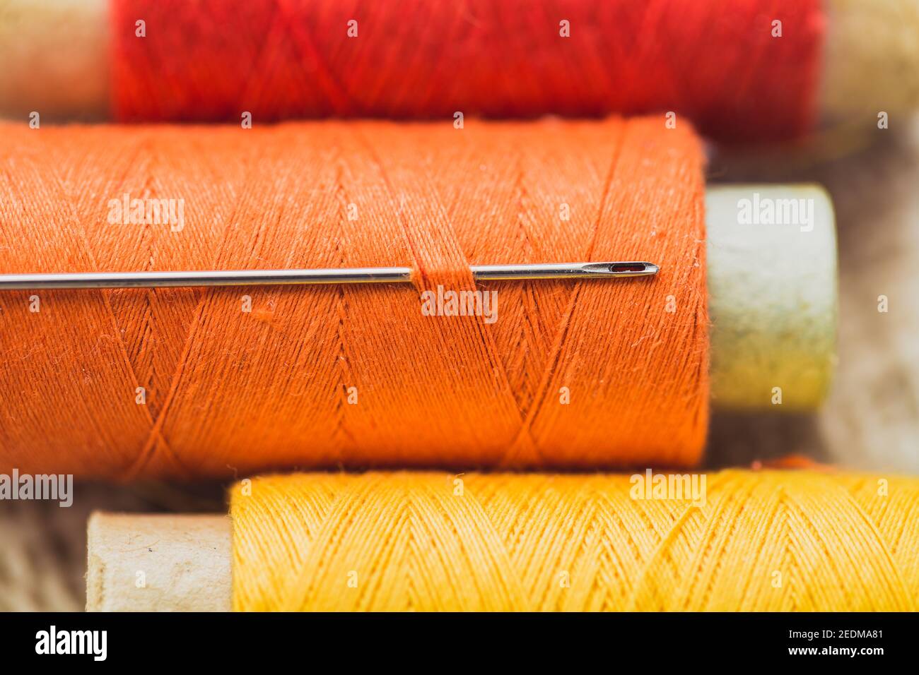 Aiguille à coudre dans une bobine de fil en orange - adapter le matériau et les outils Banque D'Images