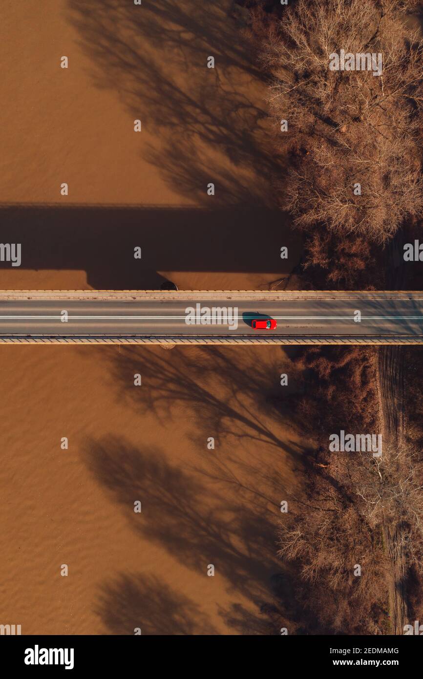 Vue aérienne d'une seule voiture rouge traversant le pont de l'autre côté de la rivière, directement au-dessus du drone pov Banque D'Images
