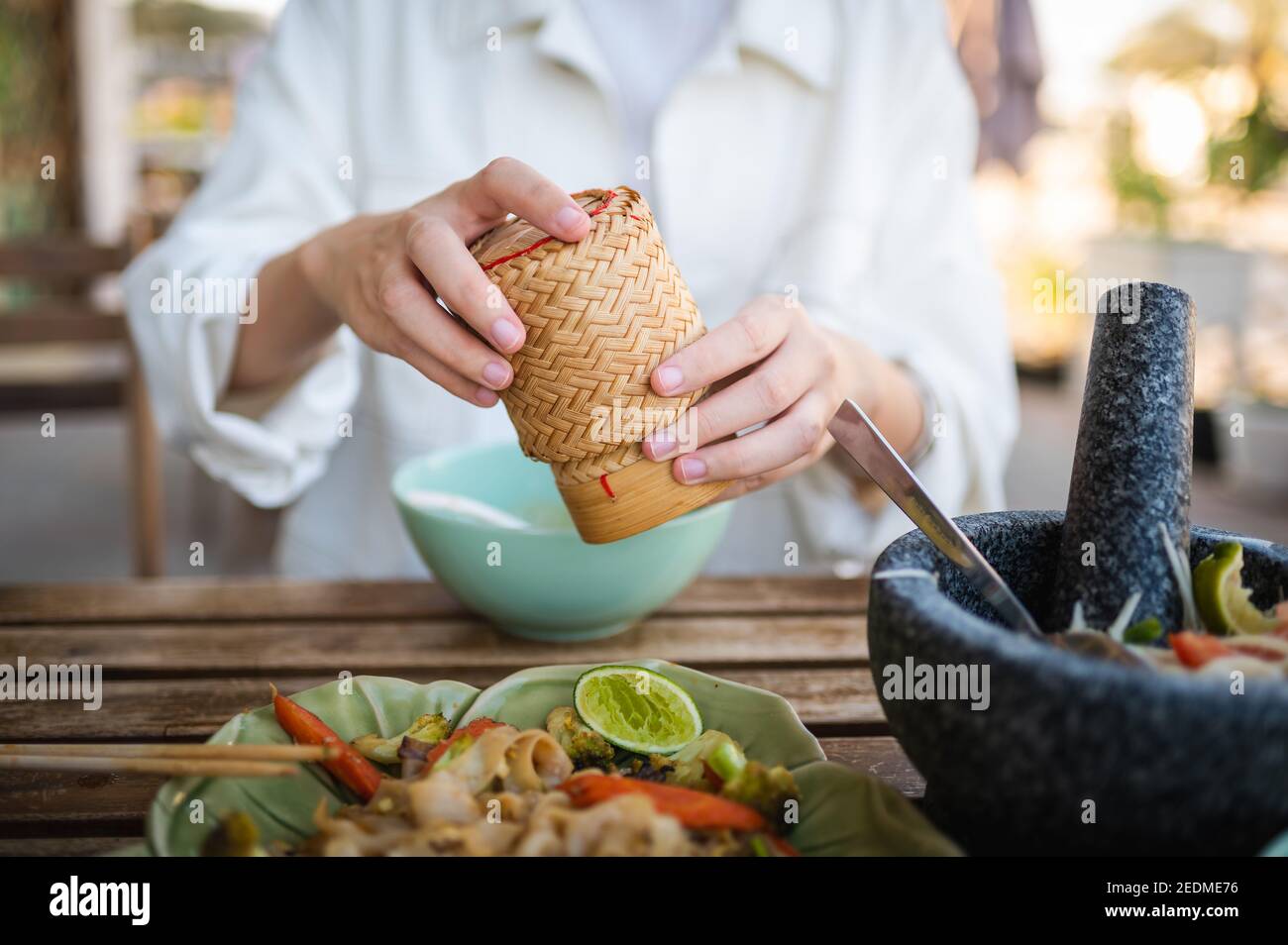 Femme ouvrant le récipient de bambou de riz collant tout en ayant un trois Repas dans un restaurant thaïlandais à proximité Banque D'Images