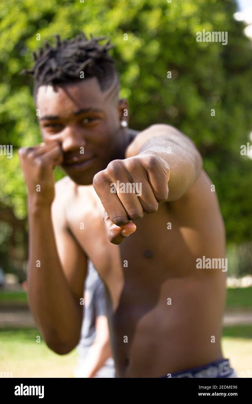 Vue avant d'un boxeur noir musclé qui se rapproche de l'appareil photo tout en souriant à l'extérieur. Concept de boxe et d'entraînement 2021. Banque D'Images