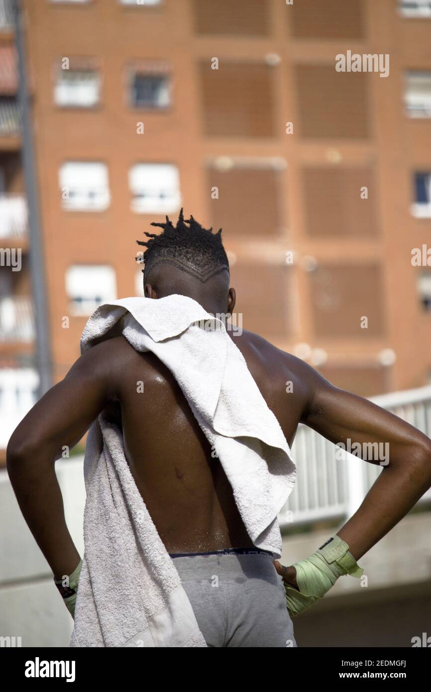 Vue arrière d'un boxer noir musclé avec un dos sueur et une serviette blanche après un entraînement physique de boxe en plein air. Concept de boxe et d'entraînement 2021. Banque D'Images