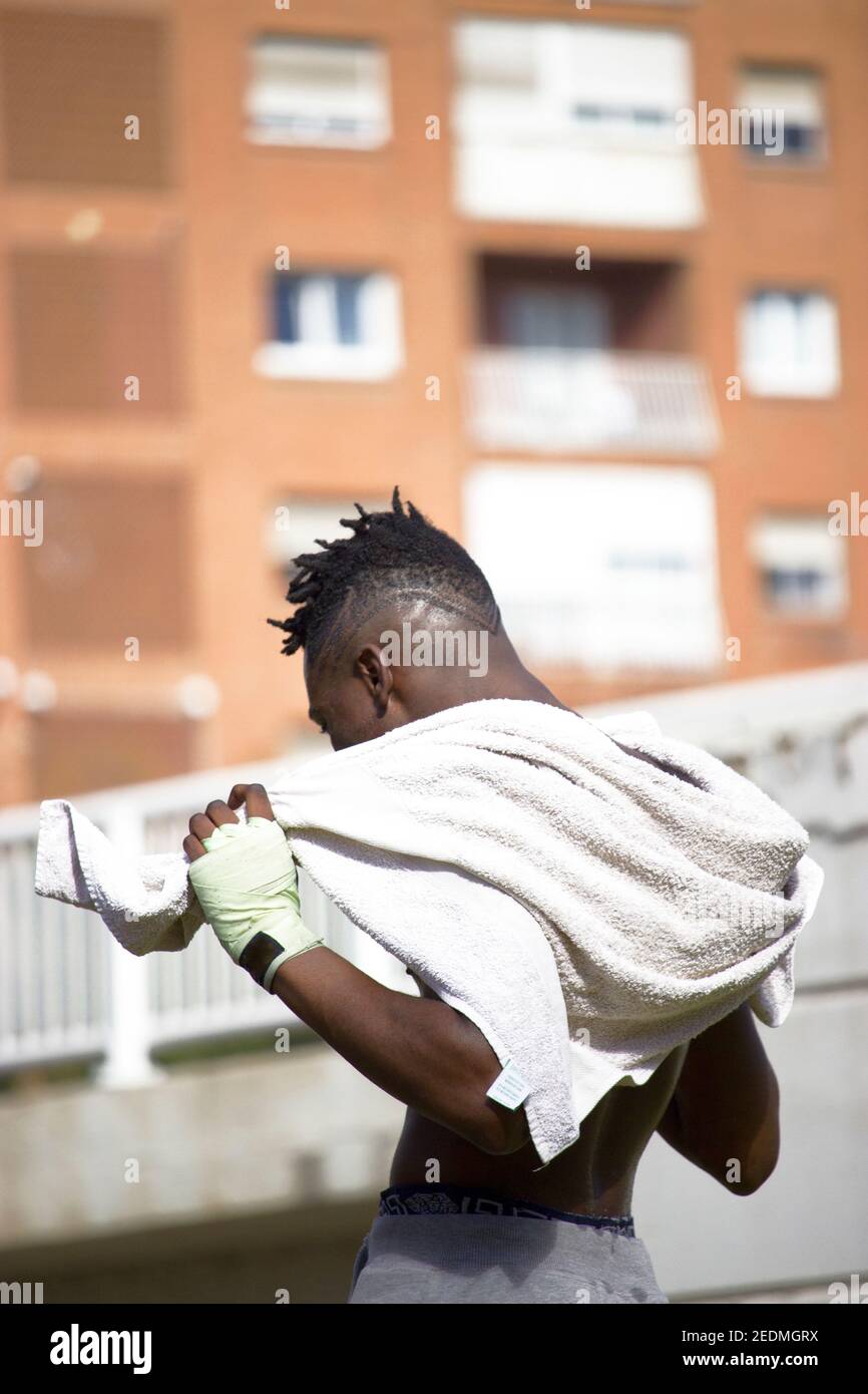 Vue arrière d'un boxer noir musclé avec un dos sueur et une serviette blanche après un entraînement physique de boxe en plein air. Concept de boxe et d'entraînement 2021. Banque D'Images