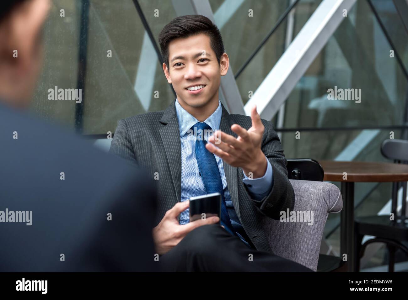 Un jeune homme d'affaires chinois asiatique beau assis et parlant avec lui partenaire dans le café Banque D'Images