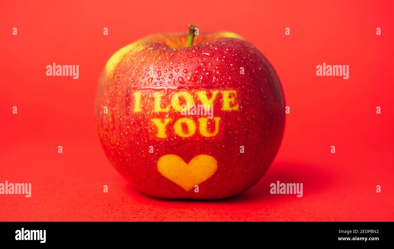 Pomme sur le thème de la Saint-Valentin avec je vous aime message et un symbole de coeur recouvert de gouttelettes d'eau et placé dessus un arrière-plan rouge Banque D'Images