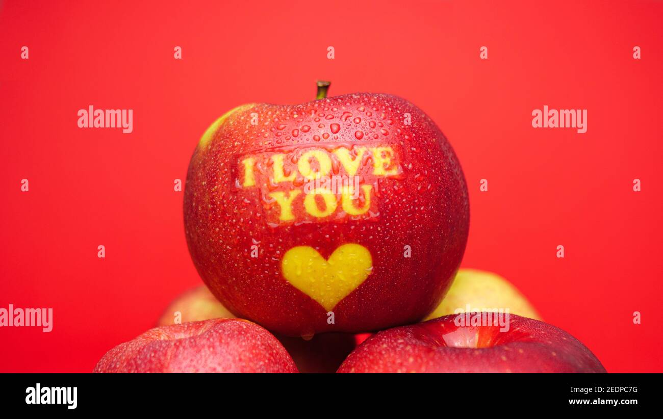 Pomme sur le thème de la Saint-Valentin avec je vous aime message et un symbole de coeur recouvert de gouttelettes d'eau et placé dessus un arrière-plan rouge Banque D'Images