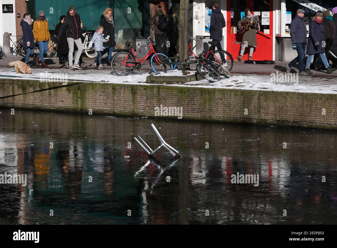 Une chaise tombée est vue sur un canal gelé alors que les gens marchent dans une rue enneigée le 13 février 2021 à Leiden, aux pays-Bas. (Photo de Yuriko Nakao/AFLO) Banque D'Images