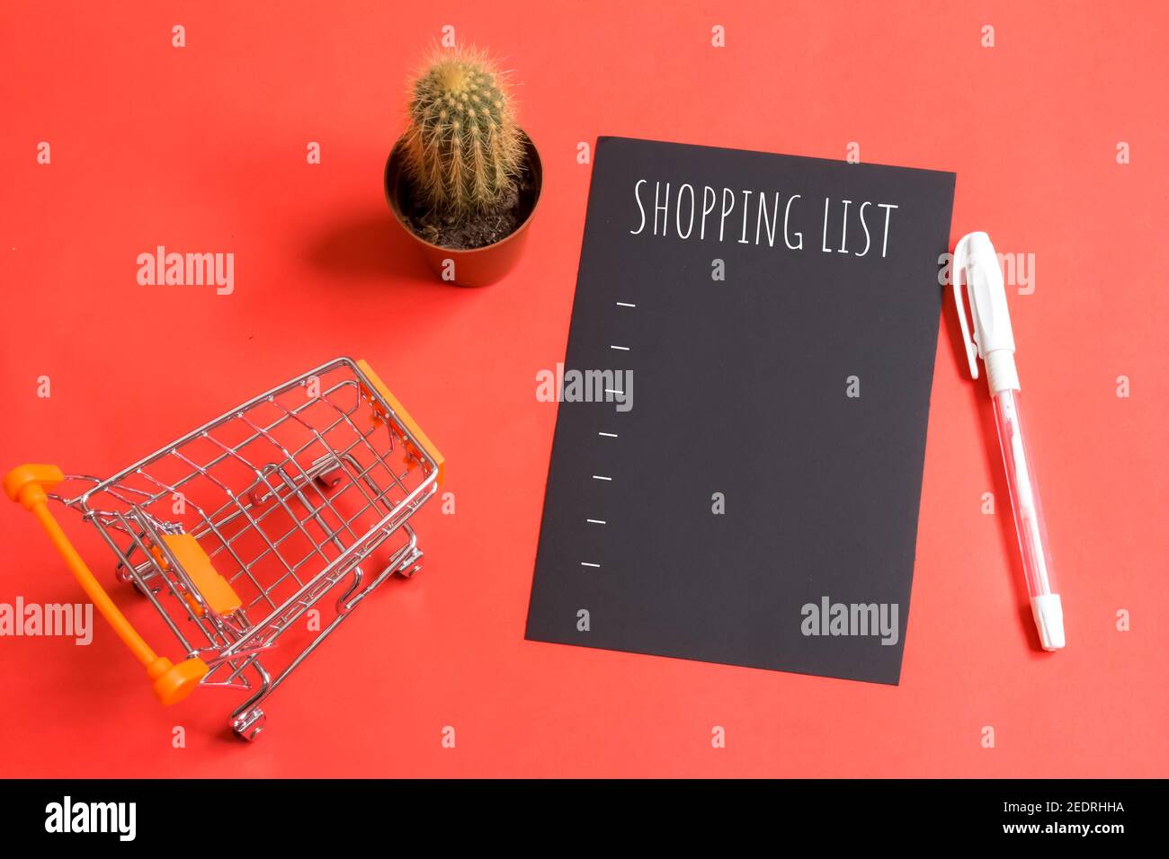 Liste d'achats écrite sur papier noir. Concept de la liste de contrôle alimentaire. Copier l'espace. Isolé sur fond rouge. À côté de la liste se trouve le mini panier. Banque D'Images