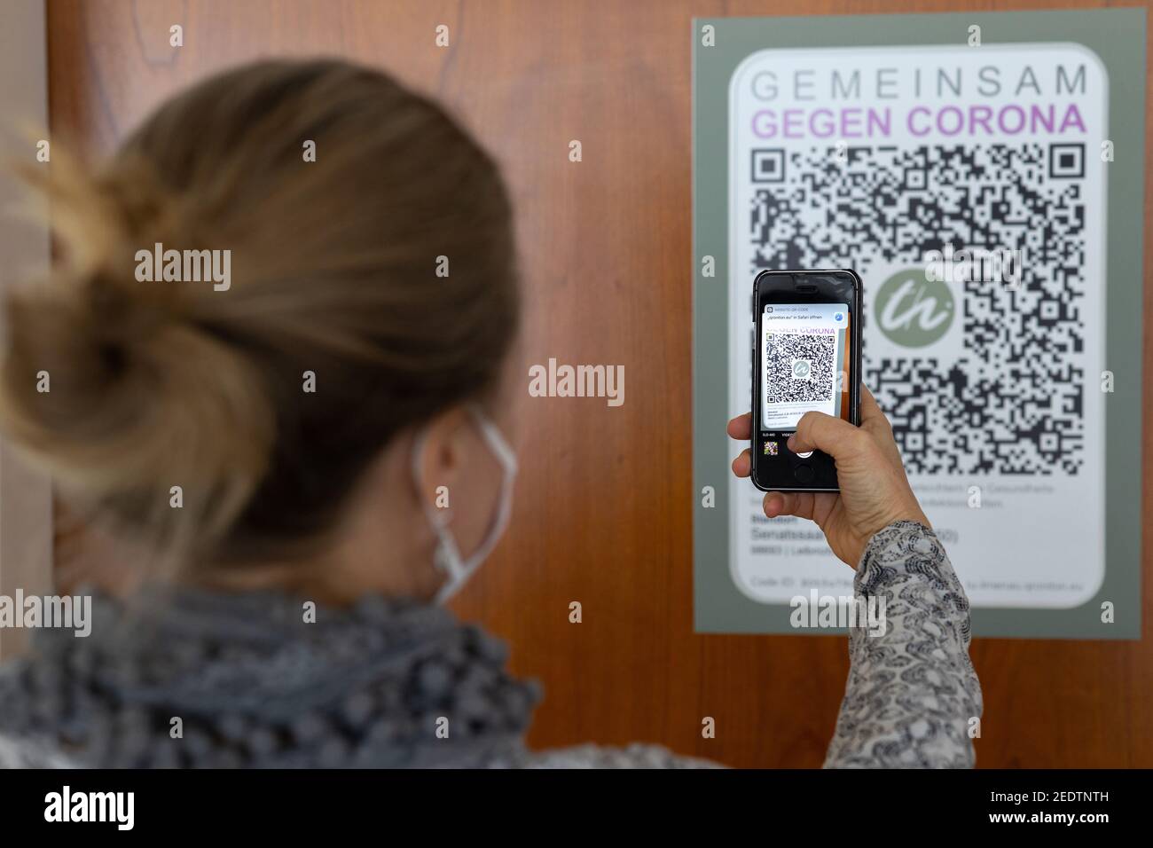 Ilmenau, Allemagne. 15 février 2021. Une femme utilise son smartphone pour scanner un code QR sur la porte du Sénat de l'Université de technologie d'Ilmenau pour un système de recherche de contact numérique. Le système QRONITON est conçu pour permettre de suivre rapidement les personnes-ressources en cas d'infection et de les signaler au service de santé publique. À cette fin, des panneaux avec le code QR de la salle respective ont été placés dans toutes les salles de conférence centrales et les salles d'enseignement à côté des entrées et sur les premiers sièges inoccupés. Credit: Michael Reichel/dpa-Zentralbild/dpa/Alay Live News Banque D'Images