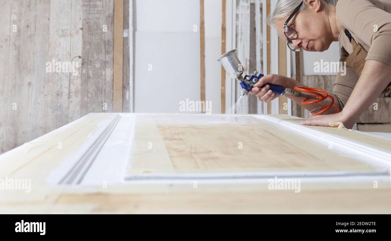 artisanat en bois, femme artisan charpentier peinture avec pistolet peinture  blanc la porte dans son atelier, portant combinaison et lunettes,  décorateur d'intérieur Photo Stock - Alamy