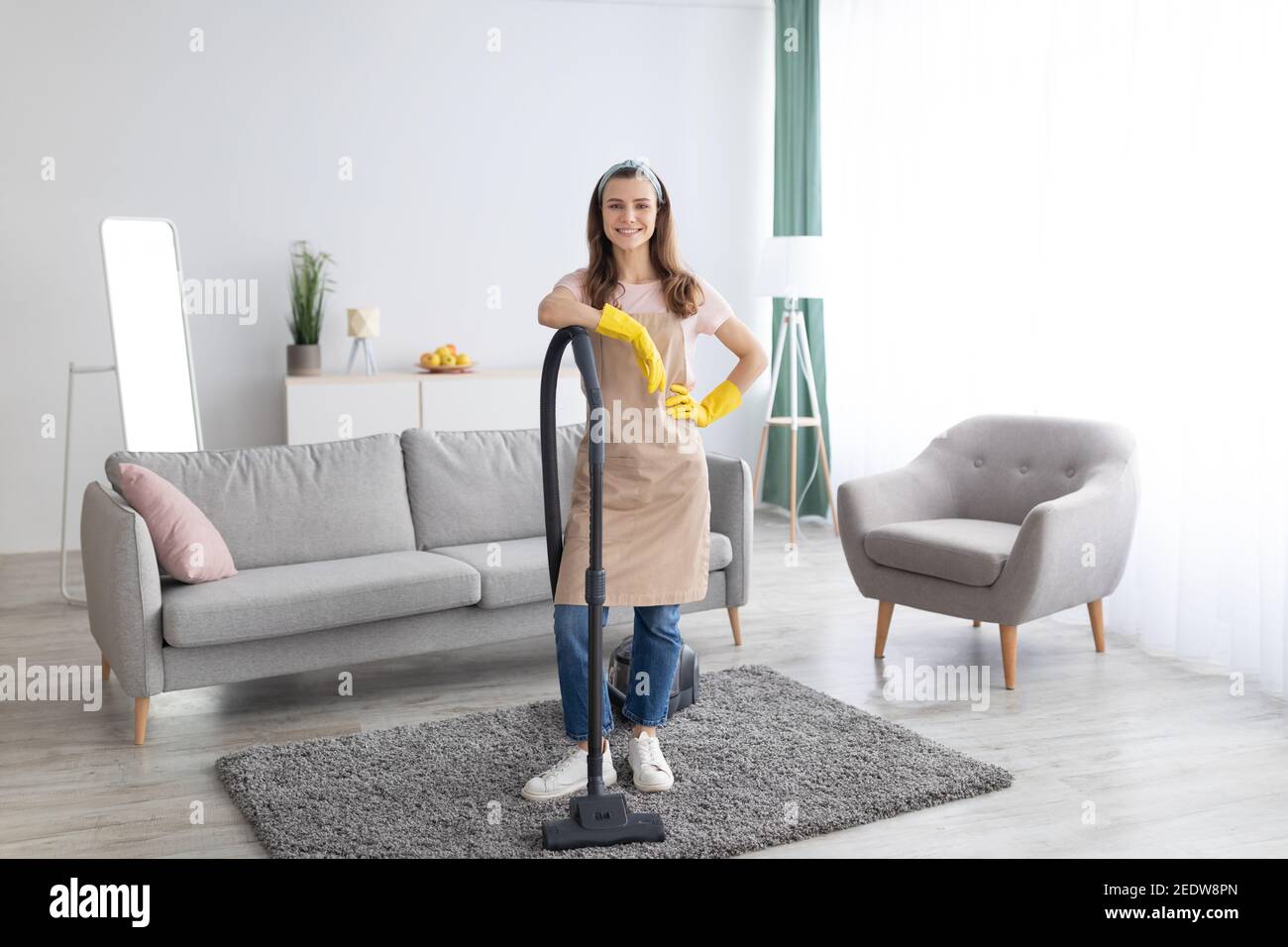 Service de ménage. Bonne jeune femme de ménage avec aspirateur au milieu d'un salon bien rangé, portrait en longueur Banque D'Images