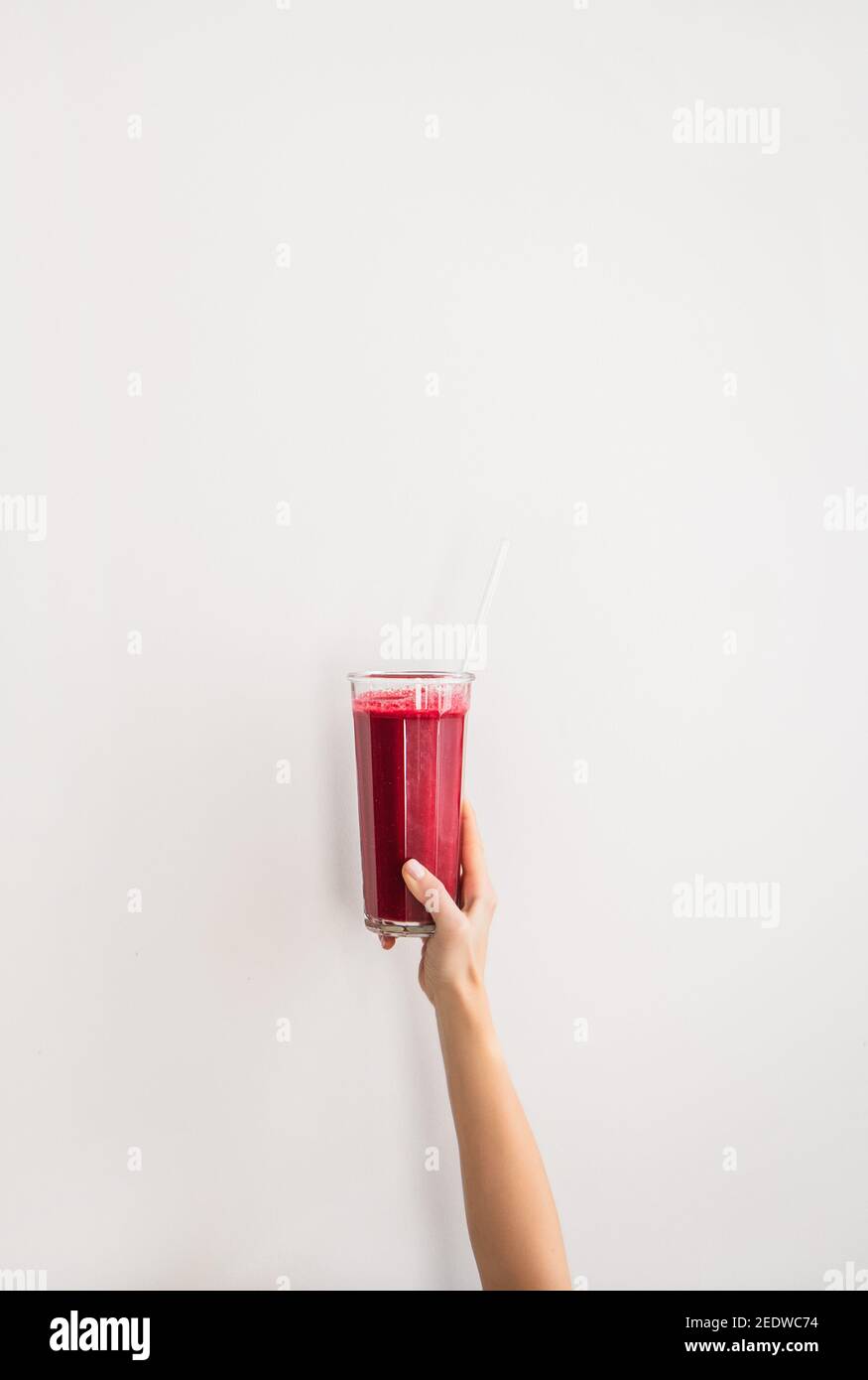 Main humaine verre tenant avec de la betterave pourpre grenade smoothie frais avec paille de verre sur fond de mur blanc, espace de copie. Détox, régime, perte de poids, concept de mode de vie sain Banque D'Images