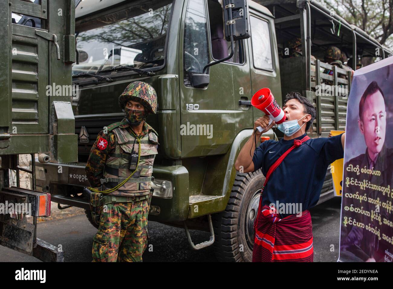 Un manifestant scanne des slogans à travers un mégaphone à côté d'un soldat debout sous la garde entre des camions militaires devant le bâtiment de la Banque centrale pendant la manifestation. L'armée birmane est arrivée ce matin sur Bank Avenue Road à Thingangyun pour faire pression sur la Banque centrale qui a rejoint le mouvement de la disobdience civile (MDP) contre le coup d'Etat militaire. Les manifestants se sont mis en place malgré la présence militaire. L'armée du Myanmar a détenu le conseiller d'État du Myanmar Aung San Suu Kyi le 01 février 2021 et a déclaré l'état d'urgence tout en prenant le pouvoir dans le pays pendant un an af Banque D'Images