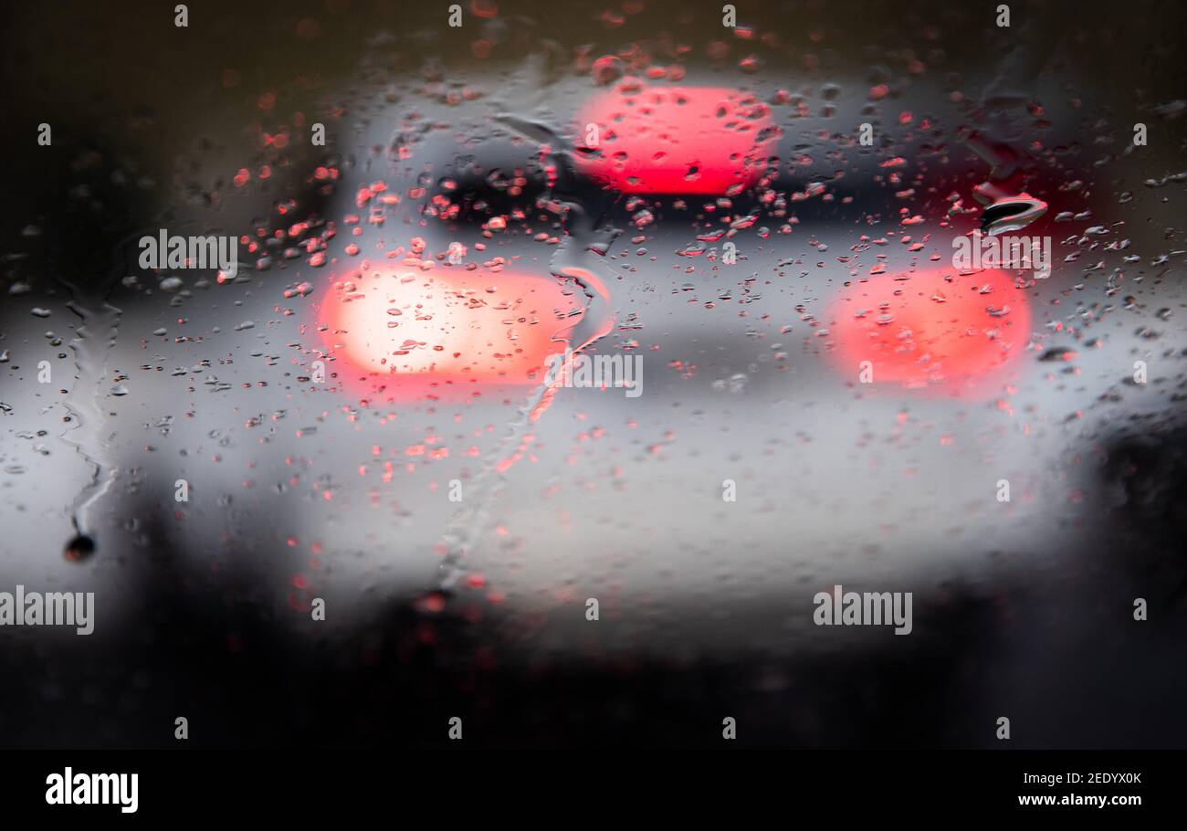 Bielefeld, Allemagne. 15 février 2021. Les gouttes de pluie se trouvent sur le pare-brise d'une voiture, tandis que les feux stop sont visibles sur le véhicule qui se trouve devant. La pluie et la boue entravent la circulation routière dans de grandes parties de la Rhénanie-du-Nord-Westphalie. Lorsque la température est proche du point de congélation, des routes glissantes peuvent se produire. Credit: Friso Gentsch/dpa/Alay Live News Banque D'Images