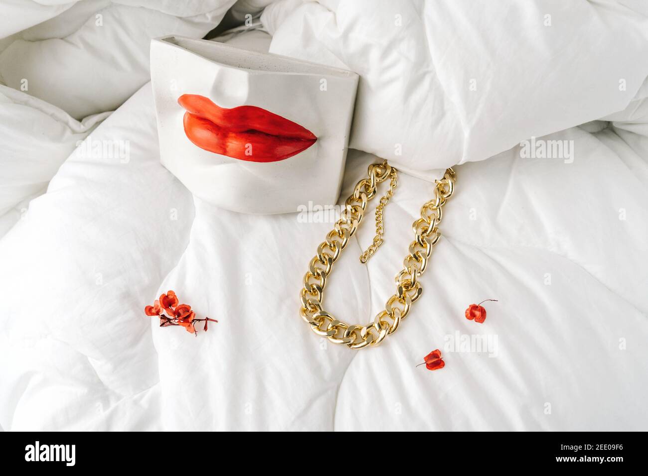 Bijoux fantaisie, chaîne de bijouterie dorée sur fond textile blanc. Les lèvres femelles en gypse blanc et les petites fleurs rouges comme la décoration. Banque D'Images