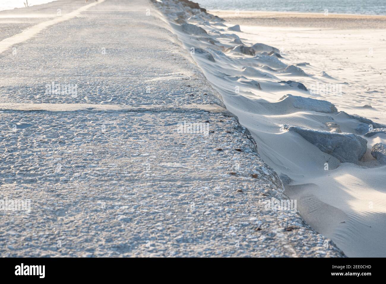 Rive de la mer avec sable blanc fin se déplaçant à travers le blizzard sur une route tarmac Banque D'Images
