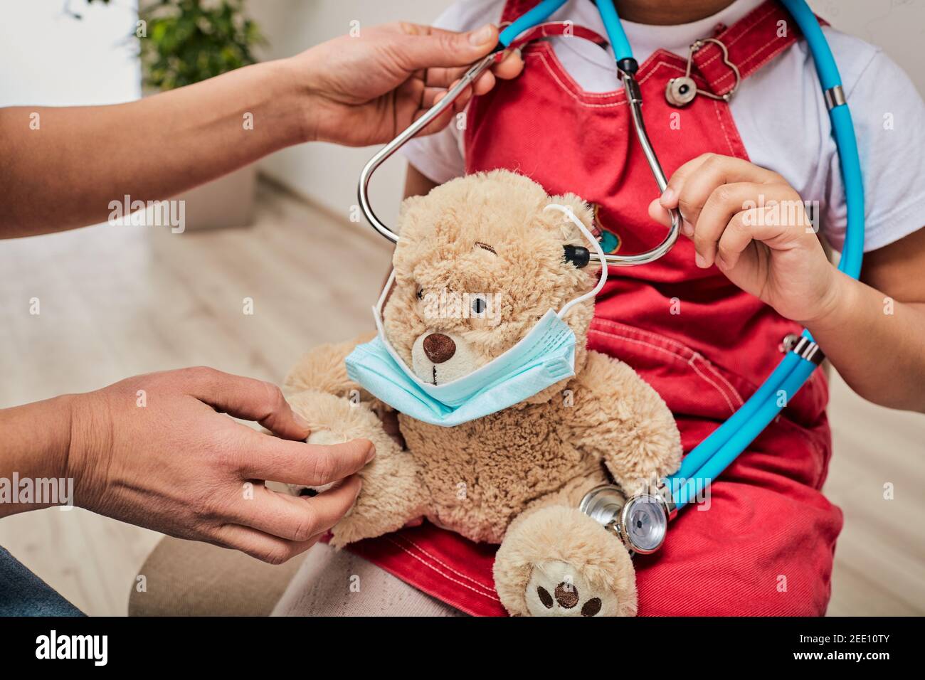 L'enfant joue avec son ours jouet avec un masque médical pendant une visite pédiatre, à l'écoute d'un stéthoscope Banque D'Images