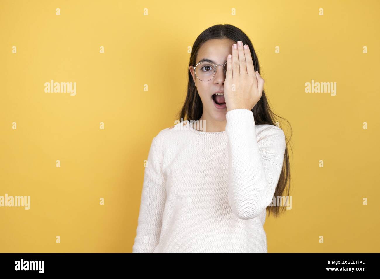 Belle fille portant des vêtements décontractés couvrant un œil avec la main, sourire confiant sur le visage et émotion surprise. Banque D'Images