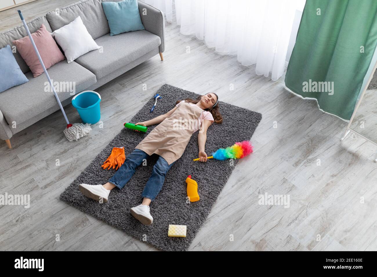 Au-dessus de la vue de la jeune femme dormant sur le sol dans la salle de séjour, entouré de fournitures de nettoyage, épuisé des travaux ménagers Banque D'Images