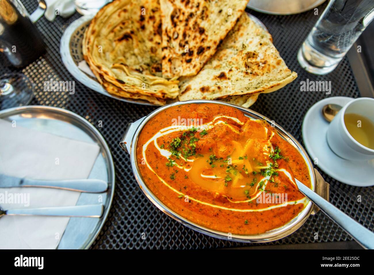 Tikka masala de poulet indien épicé dans un bol, une tasse de thé, une assiette de pain naan au beurre, un verre d'eau sur la table du restaurant. Banque D'Images