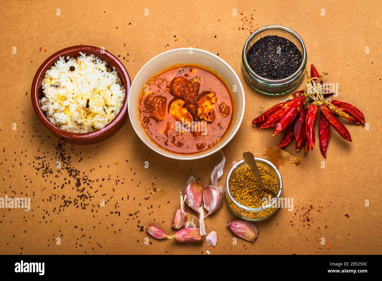Curry de Madras, riz basmati dans un petit bol, bouquet de poivrons rouges chauds secs et oignons, sésame et fenugrec en arrangemet sur fond brun. Banque D'Images