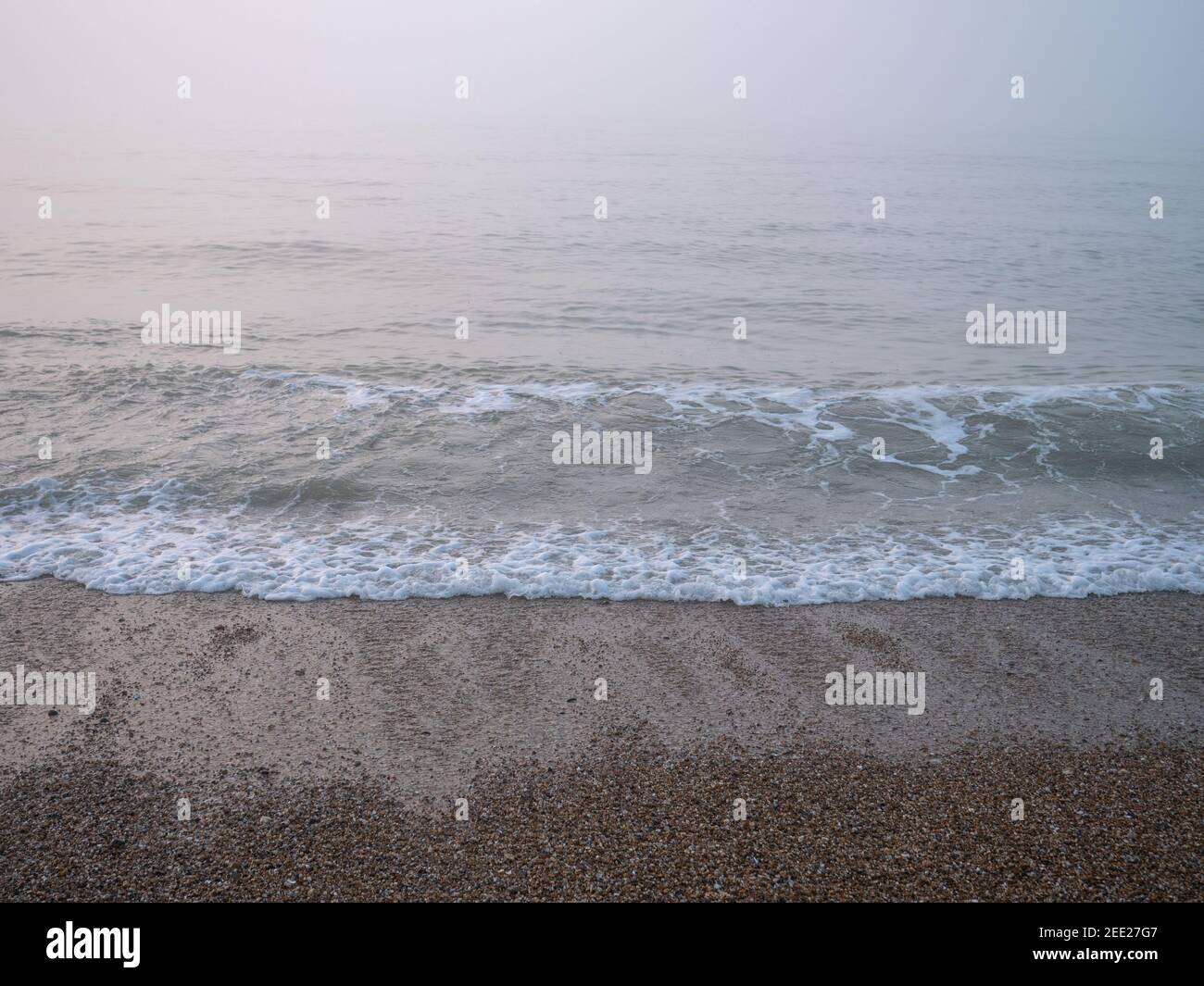 Gros plan de la vague de brises et de l'eau qui s'étire sur la plage sur la côte sud de l'Angleterre, le matin brumeux et brumeux de février. Banque D'Images