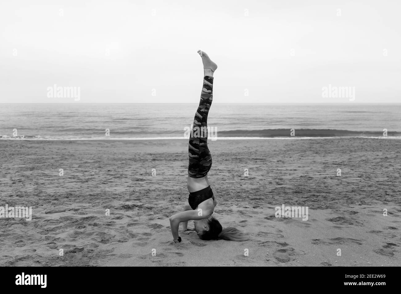 Noir et blanc Jeune tenue attrayante femme pratiquant le yoga tête pose, salamba sirsasana posture.Athletic femme travaillant dehors, à l'extérieur au beac Banque D'Images