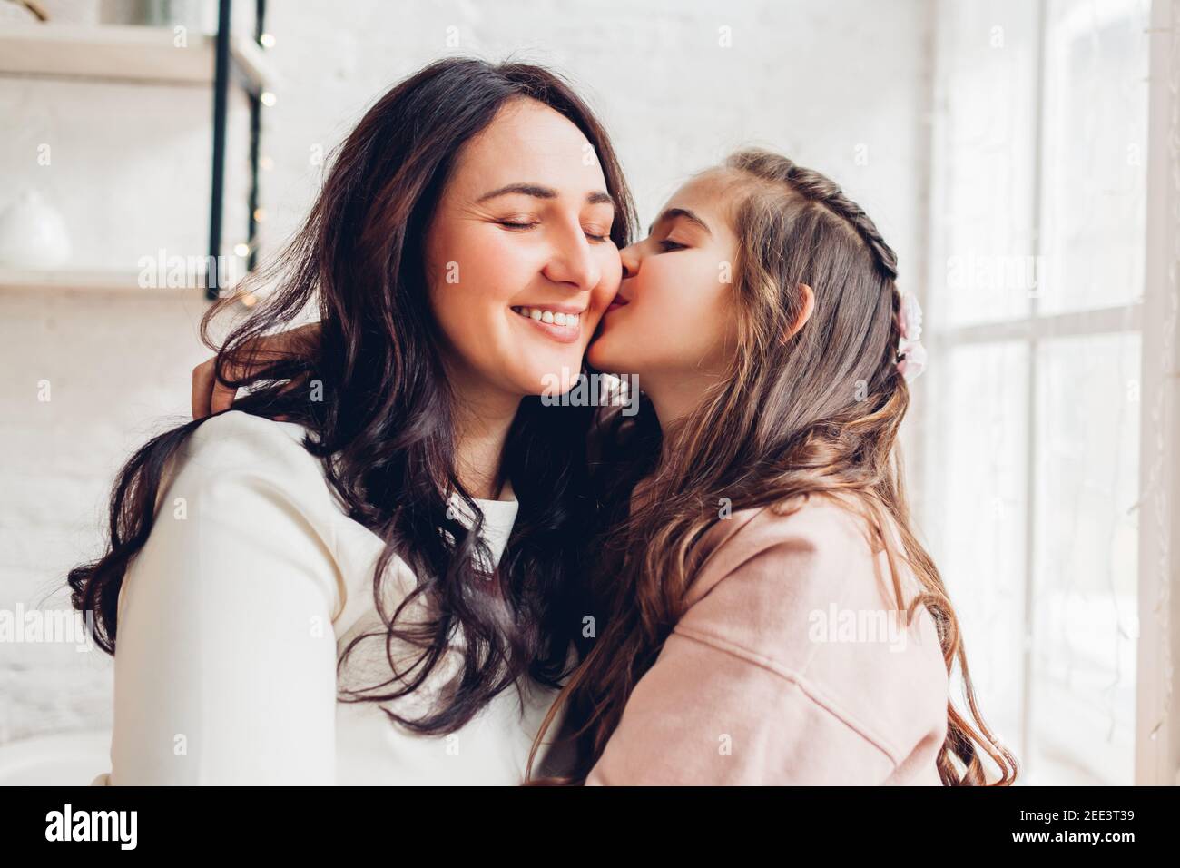 Mère et fille embrassant sur le seuil de la fenêtre de la cuisine. Fille embrassant maman sur joue. Famille ayant de bons moments ensemble à la maison. Fête des mères Banque D'Images