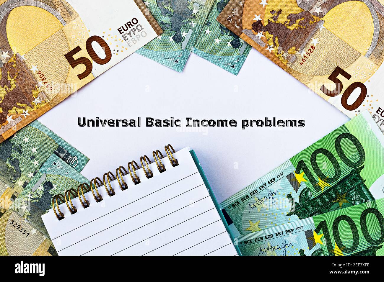 Photo TopView sur le thème du revenu de base universel. Les mots Universal Basic Income Problems, sur papier, entourés de billets et de blocs-notes en euros Banque D'Images