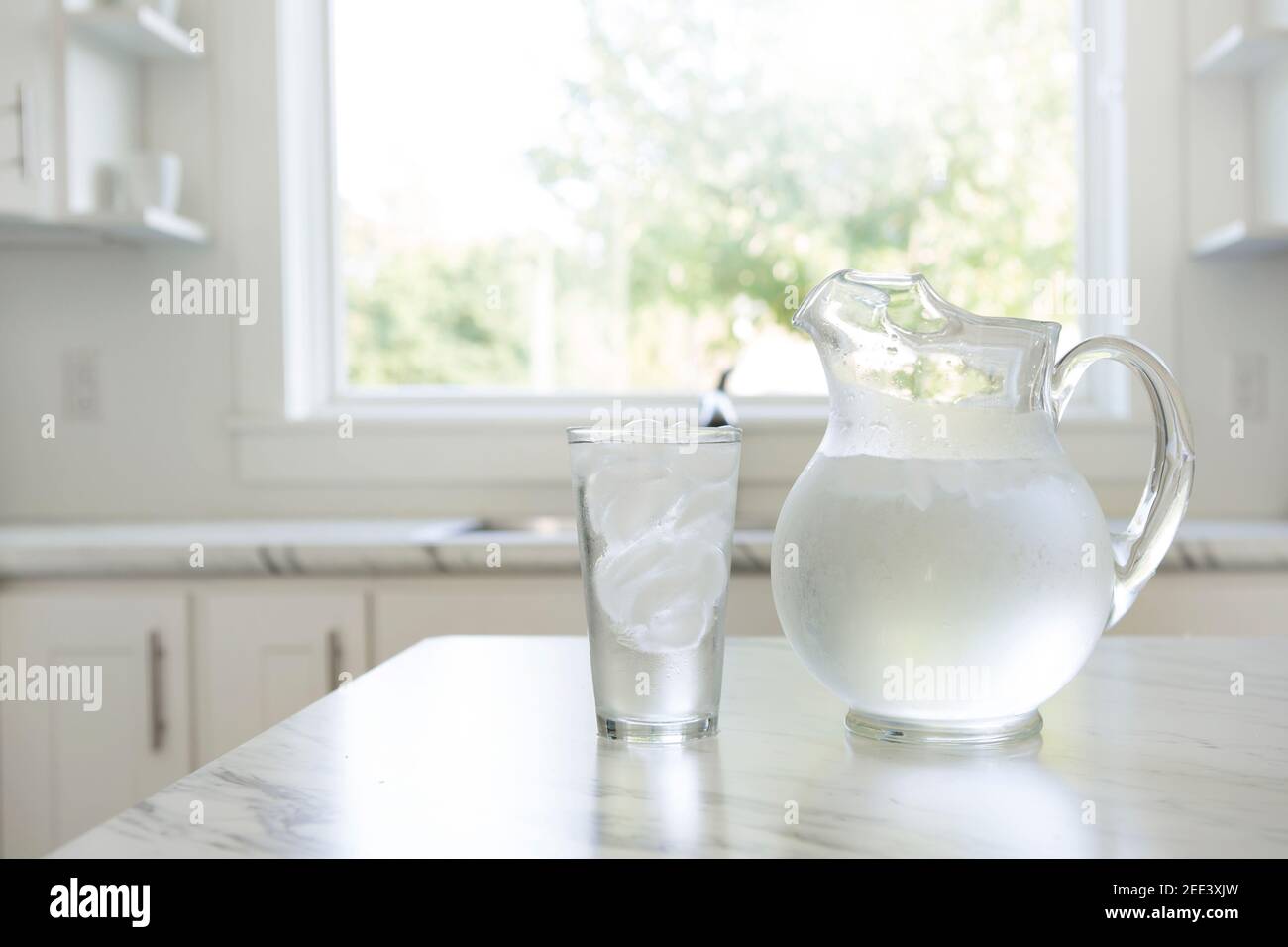 Un pichet d'eau glacée et un ensemble de verre sur un comptoir de cuisine avec lumière naturelle de fenêtre. Banque D'Images