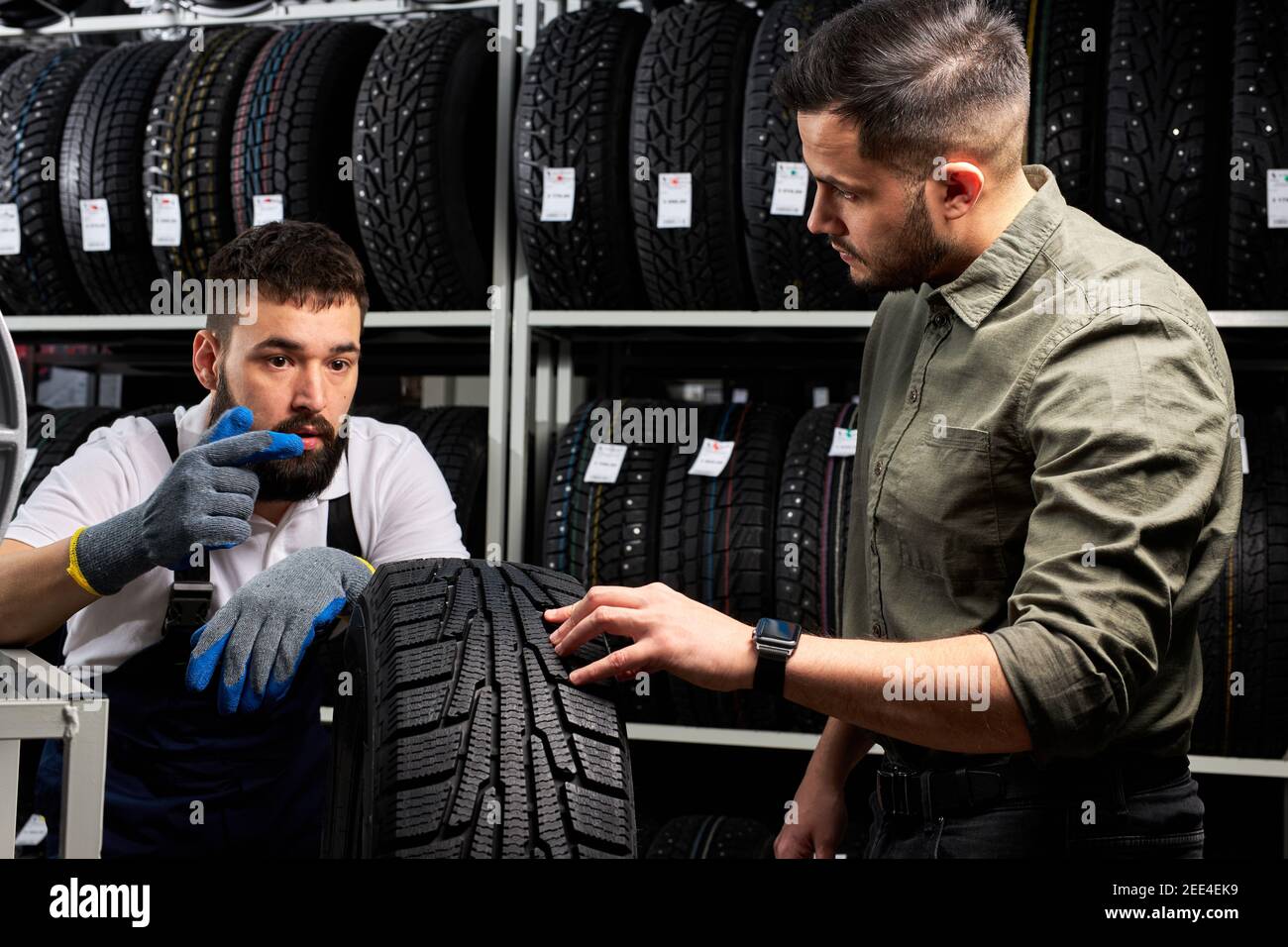 auto mécanicien parler des avantages du pneu d'auto pour le jeune client en service, l'homme est venu acheter nouveau pneu pour son automobile, stand parler et d'examiner Banque D'Images