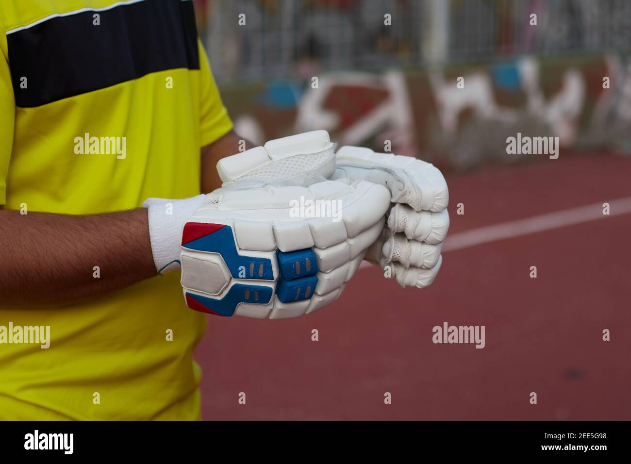 Jeune joueur de cricket avec gants blancs et uniforme jaune Banque D'Images