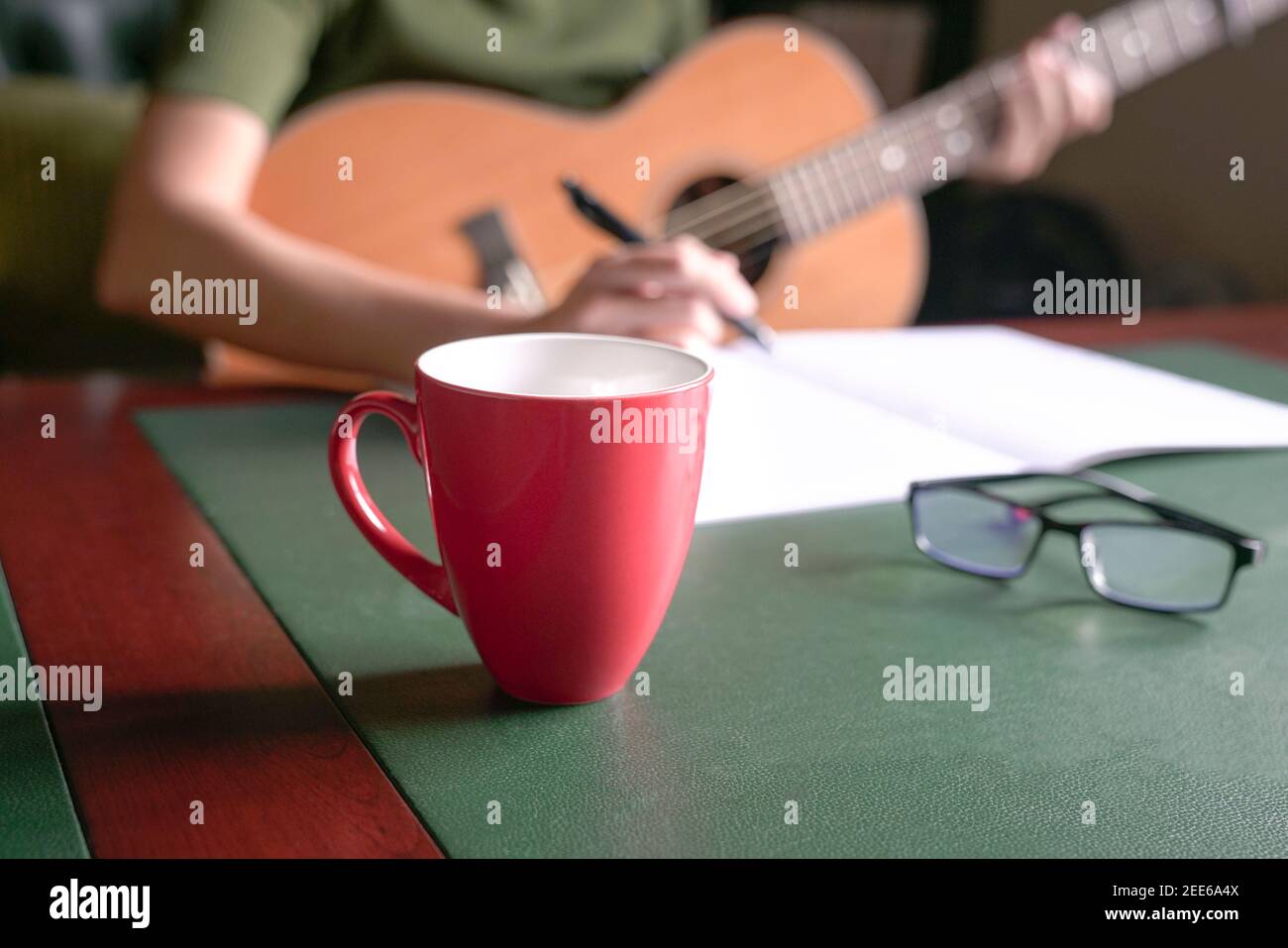 Blur femme musicienne avec guitare écrivant sur le livre au bureau. Mise au point sélective sur la tasse rouge. Banque D'Images