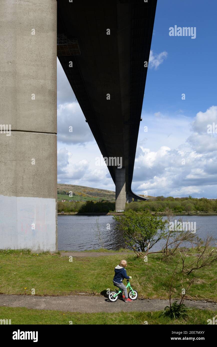 Un enfant à vélo sous le pont Erskine qui enjambe la rivière Clyde près de Glasgow, en Écosse, au Royaume-Uni Banque D'Images