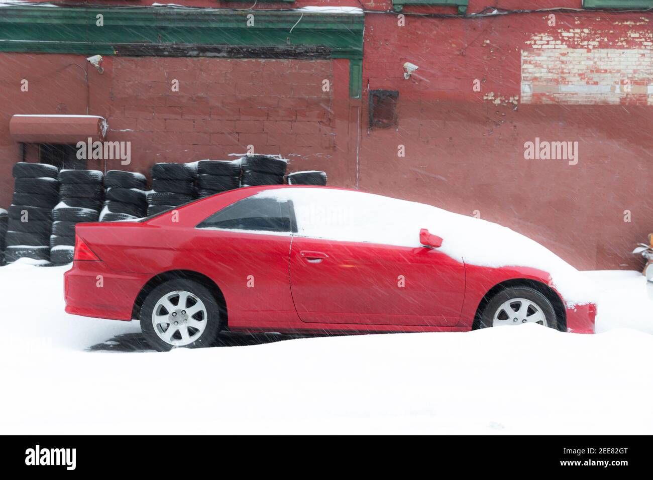 Voiture rouge recouverte de neige avec des pneus en arrière-plan sur la rue City. Sensation de neige et de circulation. Idées de travail à domicile et de télétravail. Banque D'Images