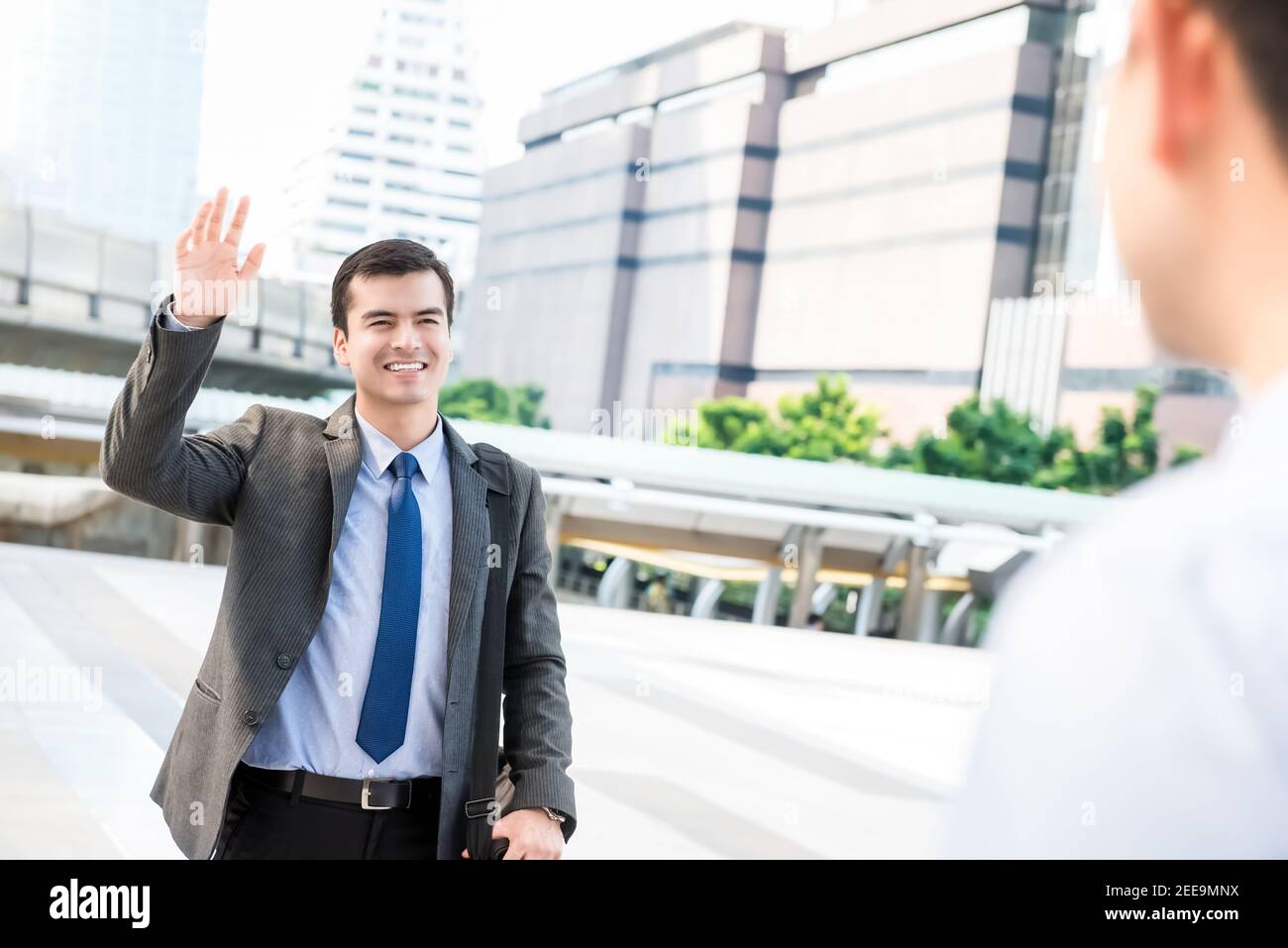 Jeune homme d'affaires charmant agitant la main saluant son ami à l'extérieur dans la ville Banque D'Images