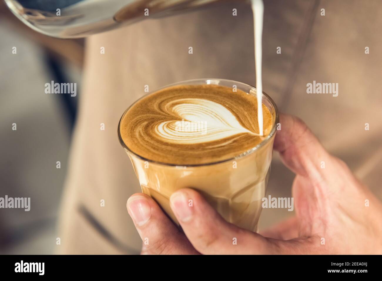 Un barista professionnel tient une tasse de café pour faire un délicieux latte en forme de cœur art Banque D'Images