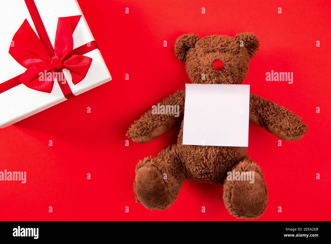 Boîte cadeau de Saint-Valentin ou de mariage et adorable poupée d'ours jouet avec carte de vœux en papier vide sur fond rouge Banque D'Images