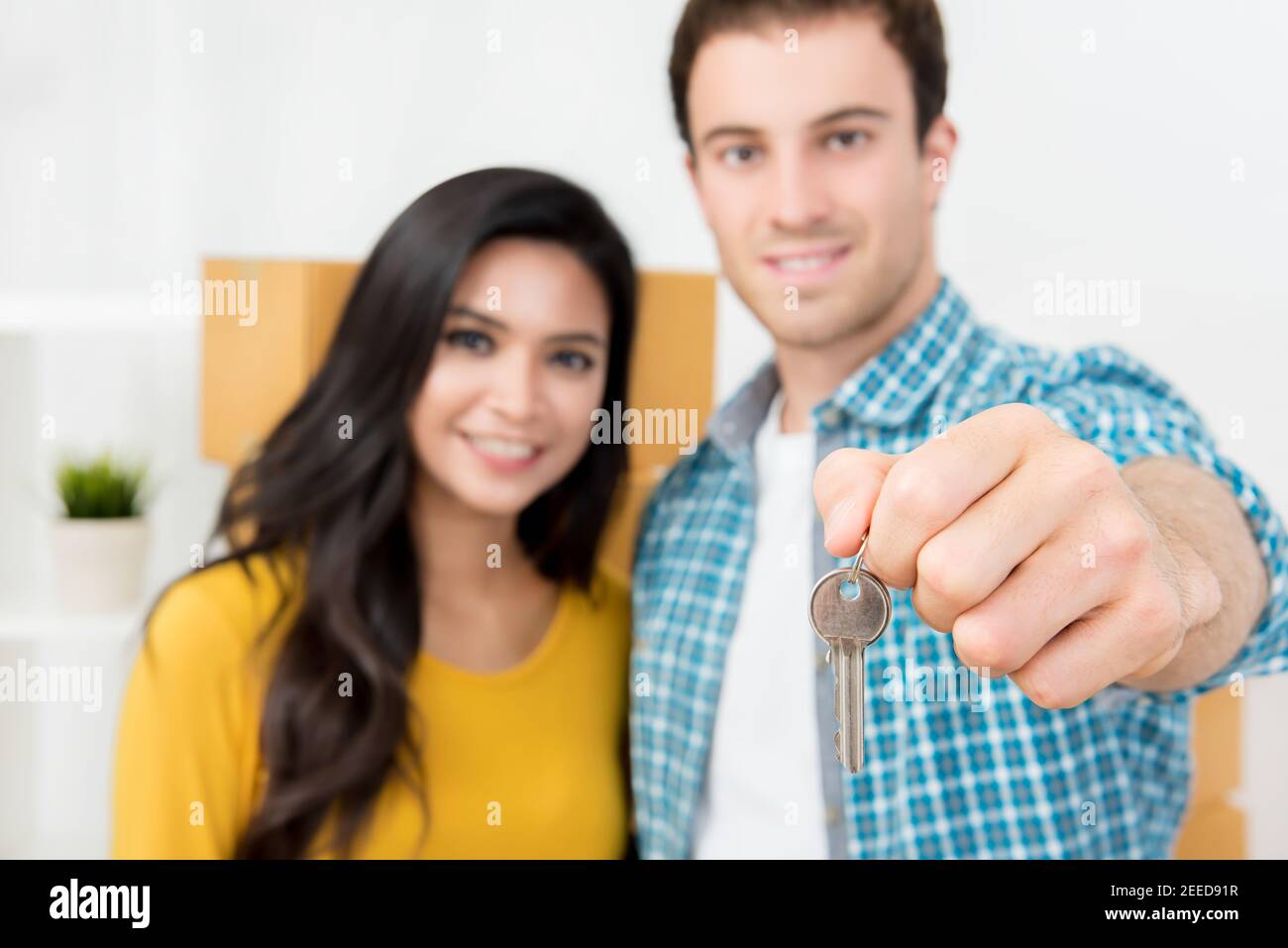 Couple interracial montrant la clé de la nouvelle maison avec des boîtes mobiles à l'arrière. Banque D'Images