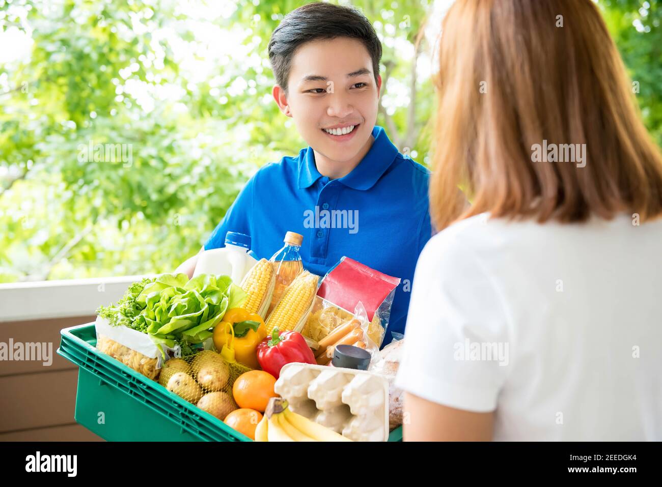 Un magasin d'alimentation asiatique delivey homme portant un poloshirt bleu livraison de nourriture à une femme à la maison Banque D'Images