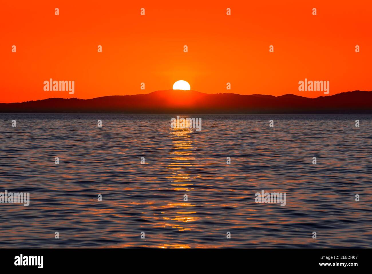 Magnifique coucher de soleil rouge sur la mer avec reflet du soleil dans l'eau et les montagnes à l'horizon, vue de la plage à Zadar, Dalmatie, Croatie Banque D'Images