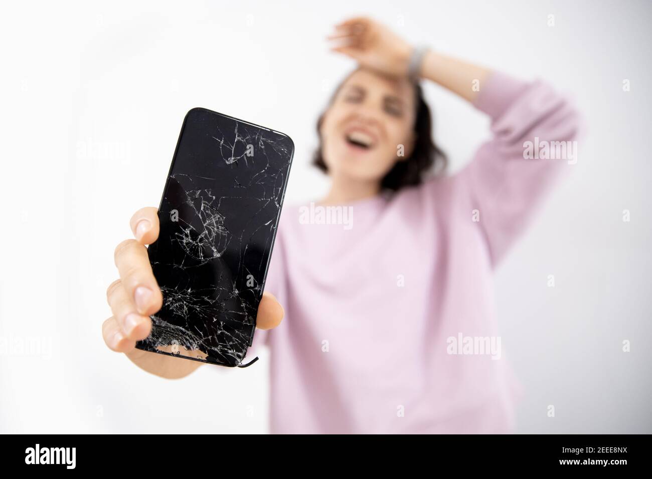 Verre cassé de l'écran du téléphone dans les mains de la jeune femme, fond blanc. Banque D'Images