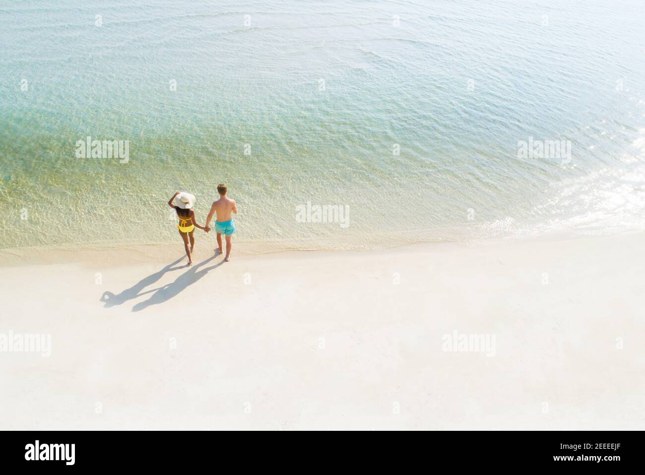 Couple de lune de miel tenant la main marcher sur la belle plage de sable blanc en été - vue sur les oiseaux Banque D'Images